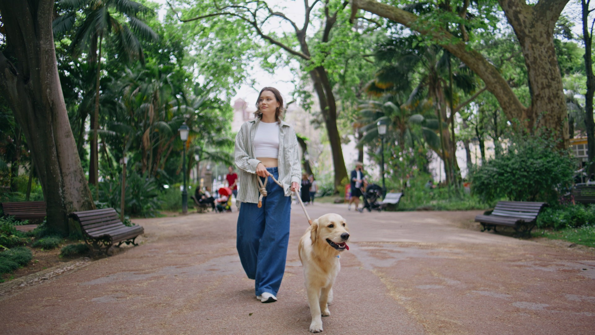 Happy girl walking dog on leash at serene park. Relaxed brunette enjoying stroll